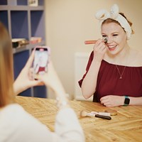 Student does her makeup while another student takes her picture